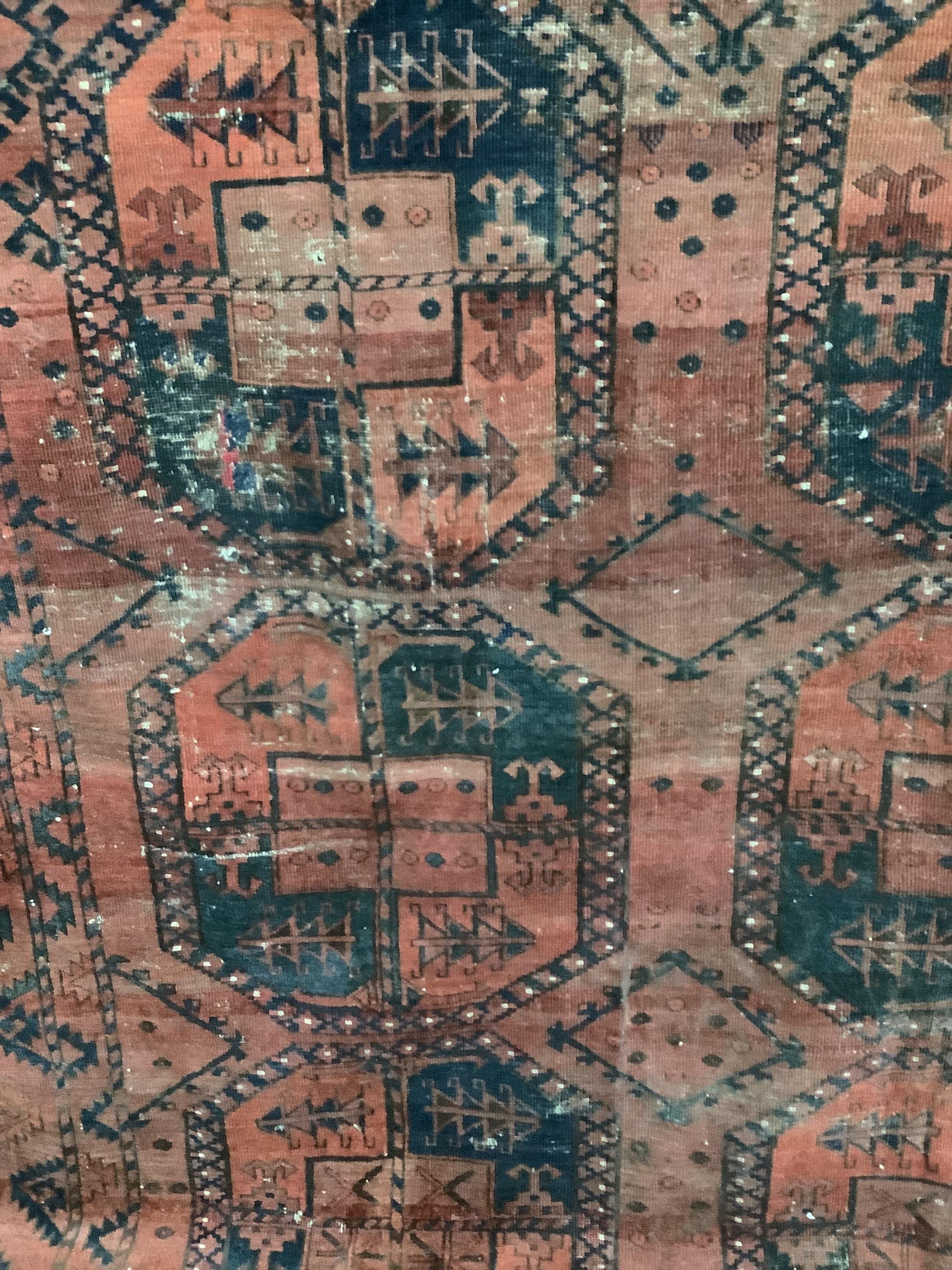 An antique Afghan red ground carpet, 340 x 278cm, worn and holed